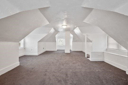 bonus room with lofted ceiling and dark colored carpet