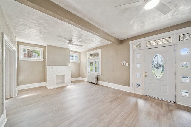 foyer entrance featuring a textured ceiling, light hardwood / wood-style flooring, a brick fireplace, ceiling fan, and radiator heating unit