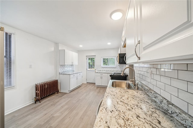 kitchen with radiator, light hardwood / wood-style floors, sink, decorative backsplash, and white cabinetry