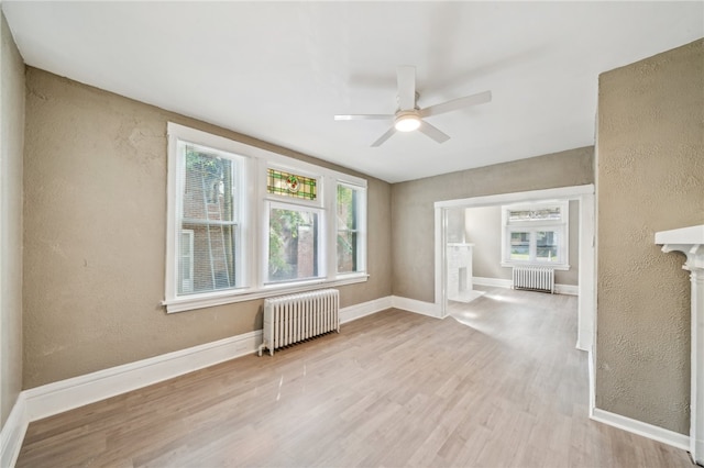 unfurnished room featuring ceiling fan, radiator, and a healthy amount of sunlight