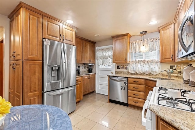 kitchen with hanging light fixtures, light tile patterned floors, light stone counters, stainless steel appliances, and sink