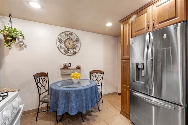 kitchen featuring stainless steel fridge with ice dispenser, light tile patterned flooring, light stone countertops, and white range