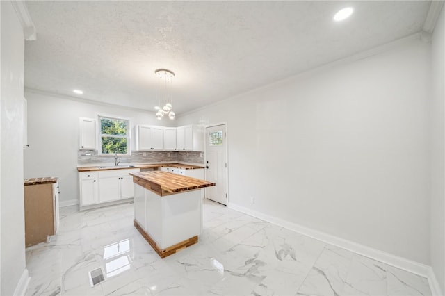 kitchen featuring decorative light fixtures, a center island, white cabinetry, and wooden counters