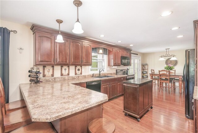 kitchen with light wood-type flooring, pendant lighting, black appliances, kitchen peninsula, and a breakfast bar