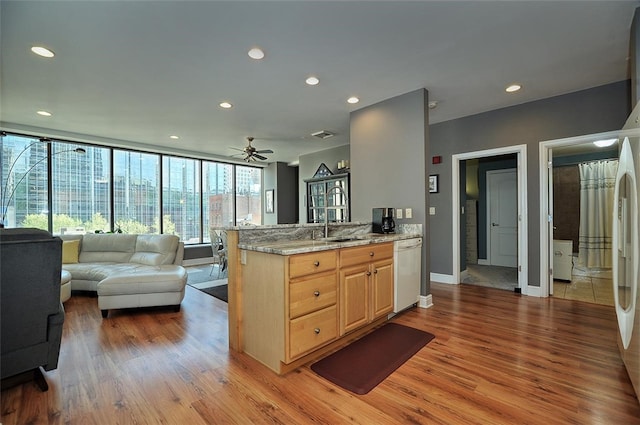 kitchen featuring light brown cabinetry, dishwasher, light stone counters, light hardwood / wood-style floors, and ceiling fan