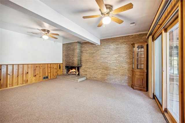 unfurnished living room with a wealth of natural light, brick wall, ceiling fan, and a brick fireplace