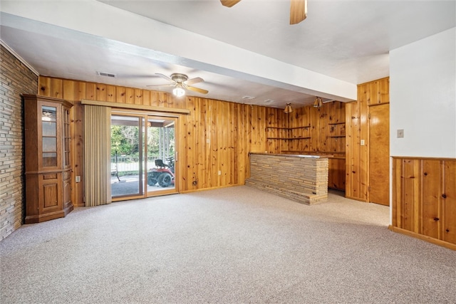 unfurnished living room featuring light carpet, brick wall, wood walls, and ceiling fan