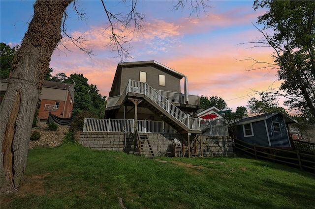 back house at dusk featuring a wooden deck and a lawn