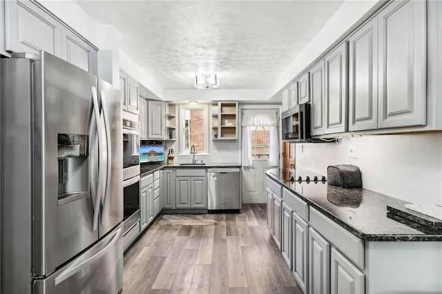 kitchen featuring gray cabinets, hardwood / wood-style floors, dark stone countertops, stainless steel appliances, and a textured ceiling