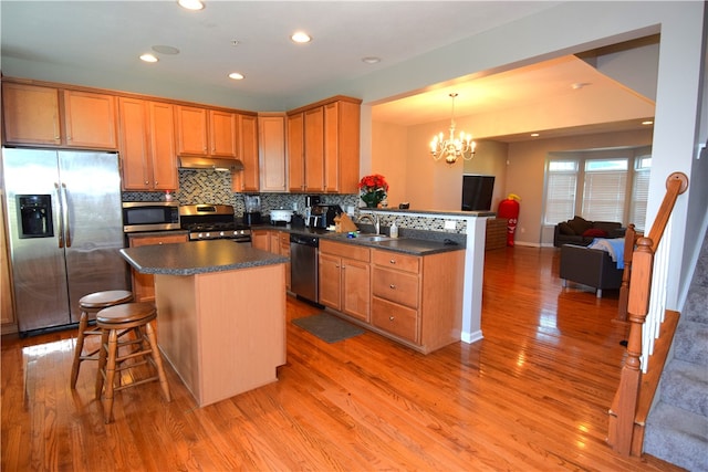 kitchen with light hardwood / wood-style floors, a breakfast bar area, sink, hanging light fixtures, and appliances with stainless steel finishes