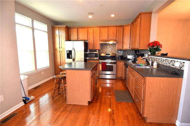 kitchen featuring a breakfast bar, a kitchen island, stainless steel appliances, hardwood / wood-style flooring, and sink