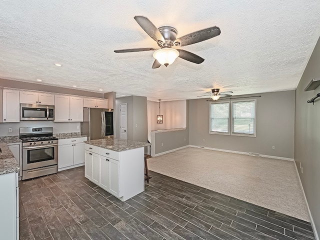 kitchen featuring light stone countertops, appliances with stainless steel finishes, a center island, ceiling fan, and white cabinets