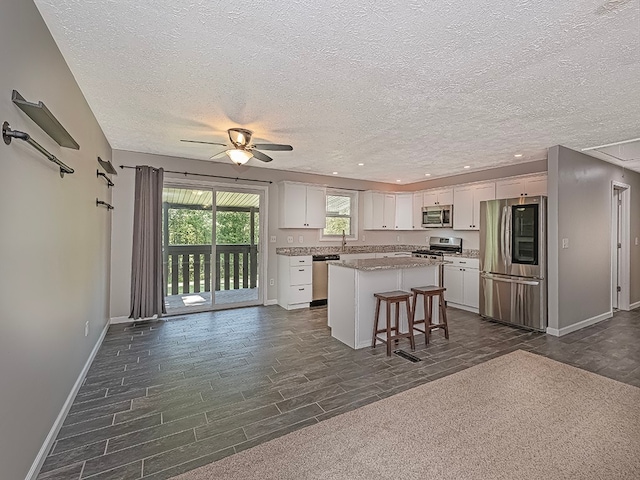 kitchen with a kitchen breakfast bar, a center island, ceiling fan, appliances with stainless steel finishes, and white cabinets