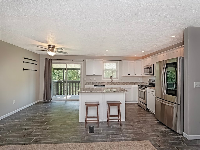 kitchen featuring a kitchen island, sink, ceiling fan, appliances with stainless steel finishes, and white cabinets