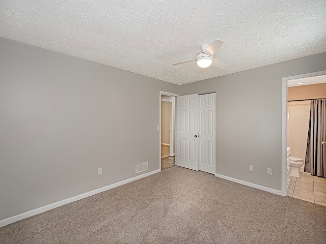 unfurnished bedroom with ceiling fan, a textured ceiling, light carpet, and ensuite bath