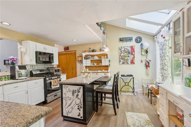 kitchen featuring light wood-type flooring, white cabinetry, stainless steel gas range oven, and a center island