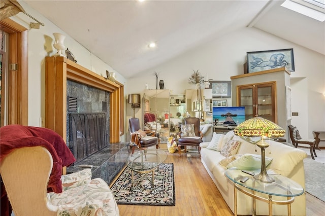 living room featuring vaulted ceiling with skylight, a fireplace, and light hardwood / wood-style floors