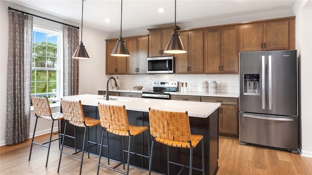 kitchen with light hardwood / wood-style flooring, appliances with stainless steel finishes, hanging light fixtures, and a breakfast bar