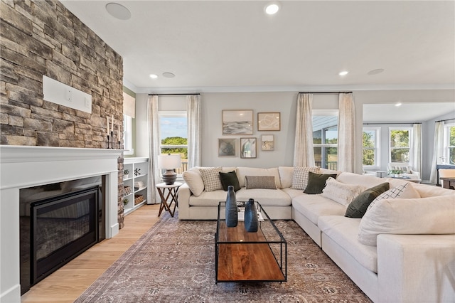 living room featuring hardwood / wood-style flooring, crown molding, and a stone fireplace