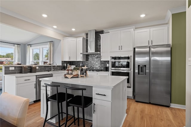 kitchen with a center island, stainless steel appliances, wall chimney range hood, and white cabinetry