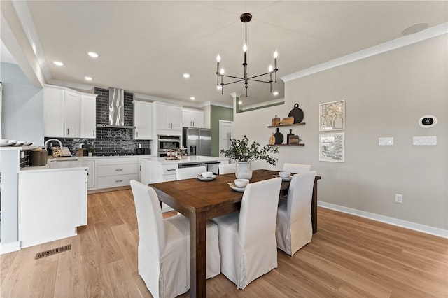 dining space featuring ornamental molding, light hardwood / wood-style flooring, a chandelier, and sink