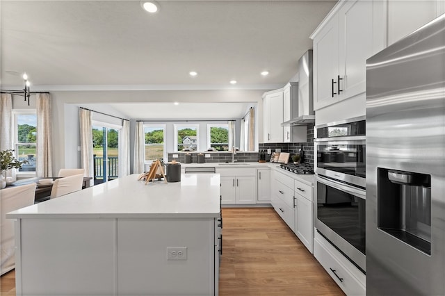 kitchen with a center island, wall chimney exhaust hood, stainless steel appliances, and white cabinets