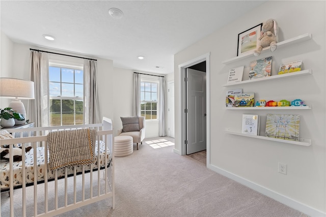 bedroom with a nursery area, light carpet, and multiple windows