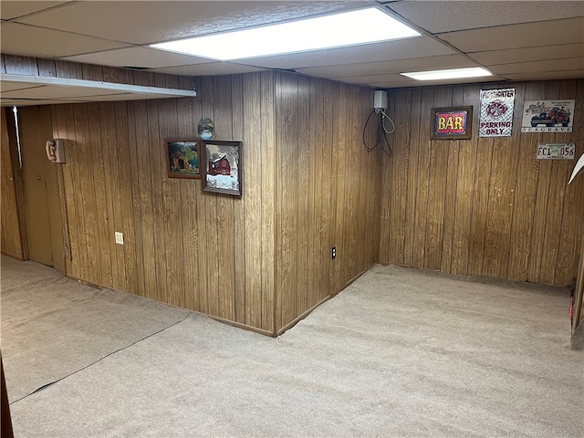 basement with light carpet, wooden walls, and a drop ceiling