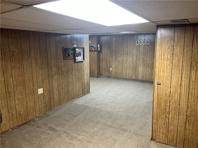 basement with light carpet, wooden walls, and a drop ceiling