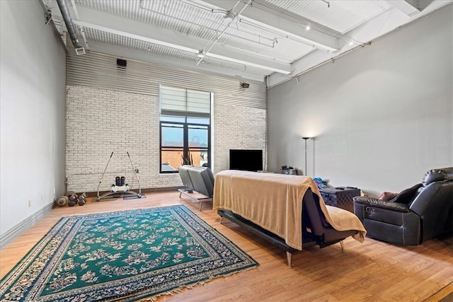 interior space featuring wood-type flooring, brick wall, a high ceiling, and a large fireplace