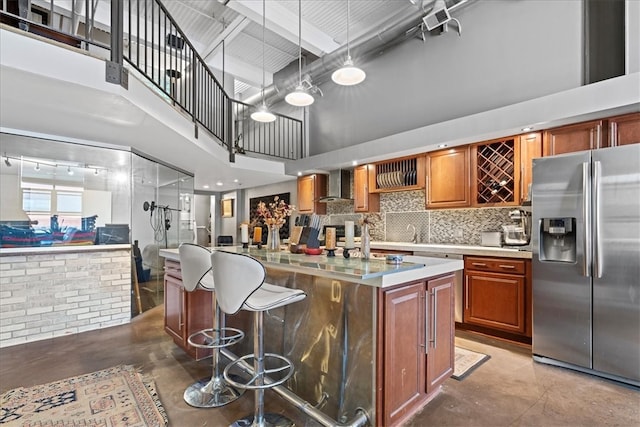 kitchen with stainless steel fridge with ice dispenser, concrete floors, decorative light fixtures, a towering ceiling, and wall chimney range hood