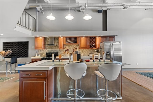 kitchen with stainless steel fridge, decorative light fixtures, wall chimney exhaust hood, a kitchen island with sink, and black stove