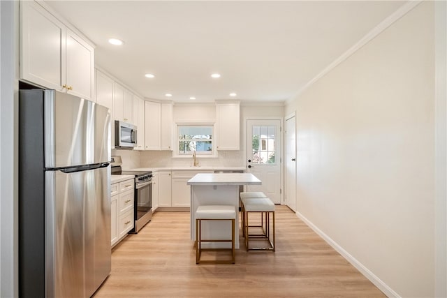 kitchen featuring a kitchen breakfast bar, appliances with stainless steel finishes, a center island, light wood-type flooring, and white cabinets