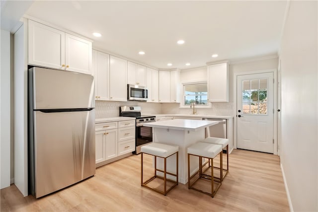 kitchen with a center island, stainless steel appliances, light hardwood / wood-style floors, white cabinetry, and a breakfast bar