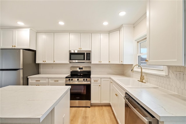 kitchen featuring light wood-type flooring, stainless steel appliances, white cabinetry, sink, and decorative backsplash