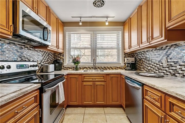 kitchen with track lighting, tasteful backsplash, light stone counters, sink, and appliances with stainless steel finishes