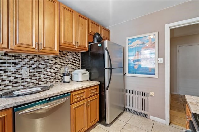 kitchen with light tile patterned floors, tasteful backsplash, stainless steel appliances, light stone counters, and radiator heating unit