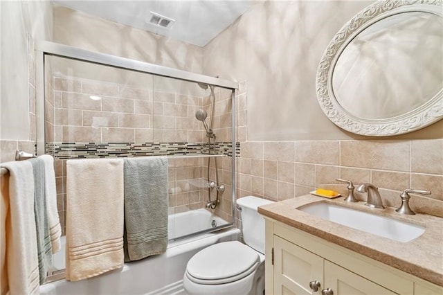 full bathroom featuring vanity, toilet, tile walls, and bath / shower combo with glass door