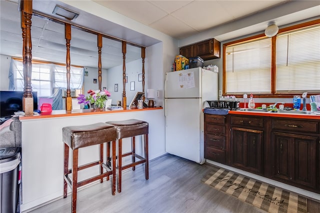 kitchen with hardwood / wood-style floors, a kitchen breakfast bar, sink, white refrigerator, and dark brown cabinetry