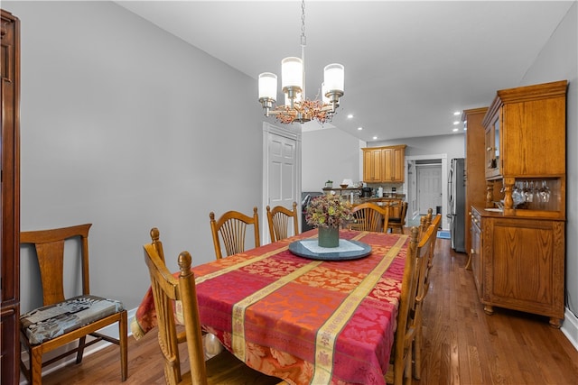 dining space featuring wood-type flooring, vaulted ceiling, and a chandelier