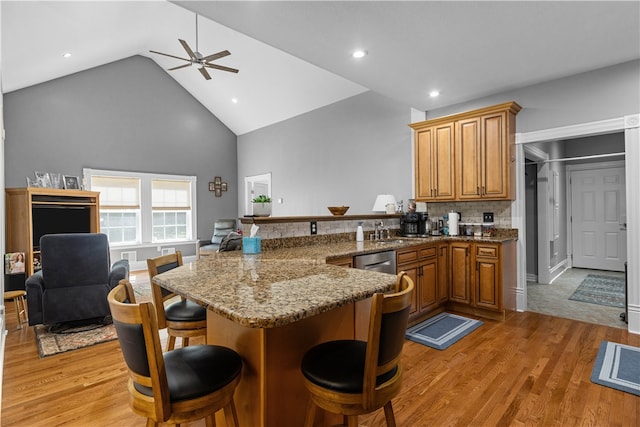 kitchen featuring high vaulted ceiling, kitchen peninsula, light wood-type flooring, a kitchen bar, and ceiling fan