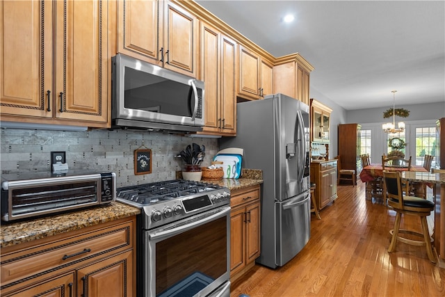 kitchen featuring hanging light fixtures, light hardwood / wood-style flooring, stone counters, a chandelier, and appliances with stainless steel finishes