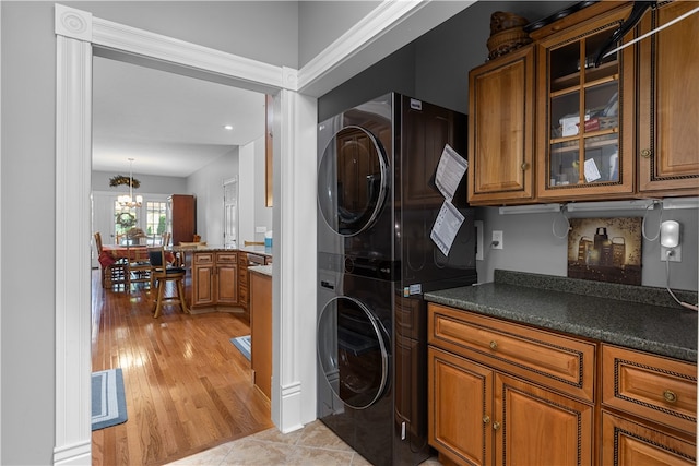 laundry area featuring an inviting chandelier, light hardwood / wood-style flooring, and stacked washer and dryer