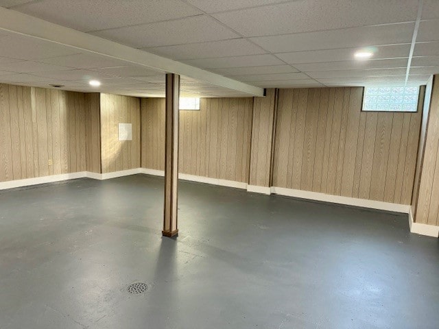 basement featuring wooden walls and a drop ceiling