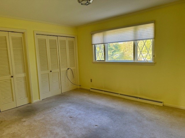 unfurnished bedroom featuring multiple closets, crown molding, a baseboard heating unit, and light colored carpet