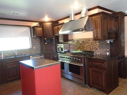 kitchen featuring decorative backsplash, wall chimney exhaust hood, stainless steel appliances, a center island, and sink