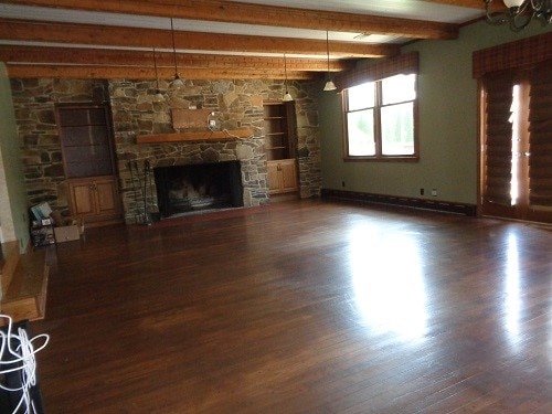 unfurnished living room with a fireplace, beam ceiling, and dark wood-type flooring