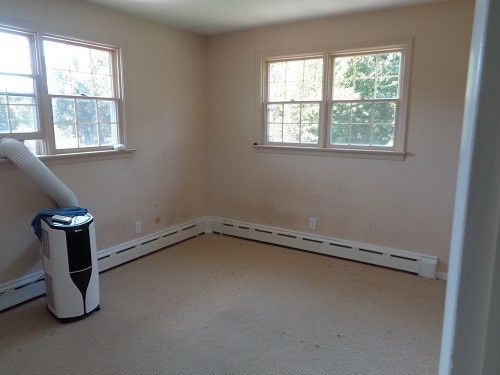 carpeted spare room featuring a baseboard heating unit and plenty of natural light