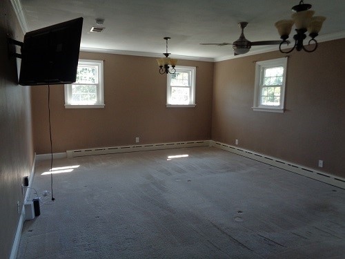 empty room with ceiling fan with notable chandelier, plenty of natural light, and baseboard heating