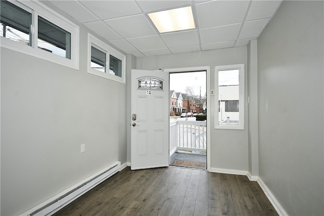 doorway to outside featuring dark wood-type flooring, baseboard heating, and a drop ceiling